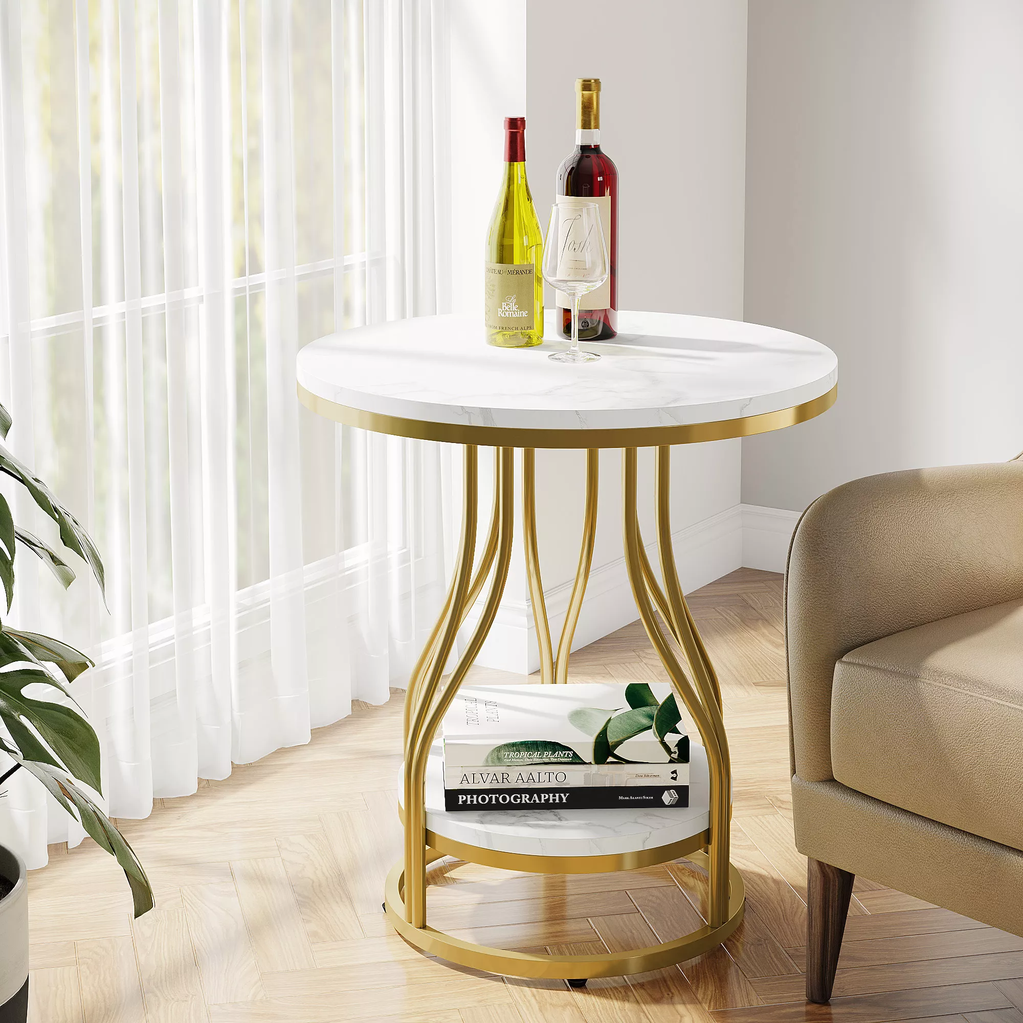 Elegant gold and white round side table with a marble top, styled with two wine bottles and a wine glass, placed beside a beige armchair and sheer curtain window.