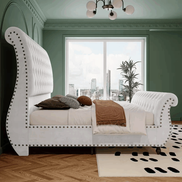 White velvet upholstered sleigh bed with tufted headboard and footboard, scroll design, and nailhead trim in a green-walled bedroom with city view.